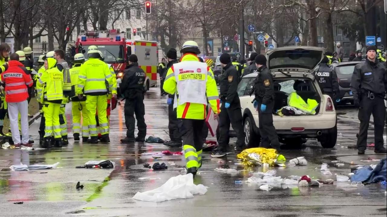 Rettungskräfte stehen am Einsatzort um ein Auto. In der Münchner Innenstadt ist ein Fahrzeug in eine Menschengruppe gefahren. Auf dem Boden liegen medizinische und persönliche Gegenstände.