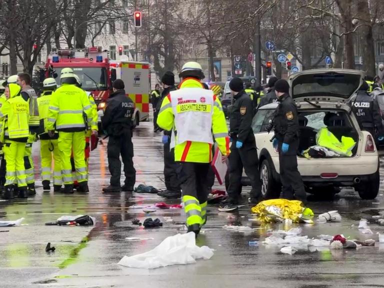 Rettungskräfte stehen am Einsatzort um ein Auto. In der Münchner Innenstadt ist ein Fahrzeug in eine Menschengruppe gefahren. Auf dem Boden liegen medizinische und persönliche Gegenstände.