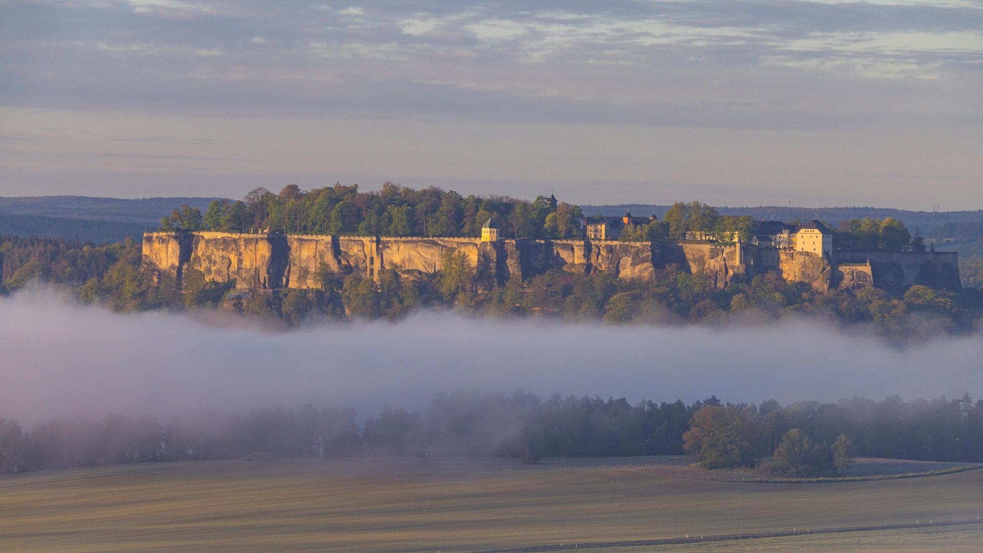Sonnenaufgang in der Sächsischen Schweiz: Die Festung Königstein im Morgennebel von der neuen Aussichtsplattform hoch über der Elbe aus gesehen. Sonnenaufgang in der Sächsischen Schweiz: Die Festung Königstein im Morgennebel von der neuen Aussichtsplattform hoch über der Elbe aus gesehen.