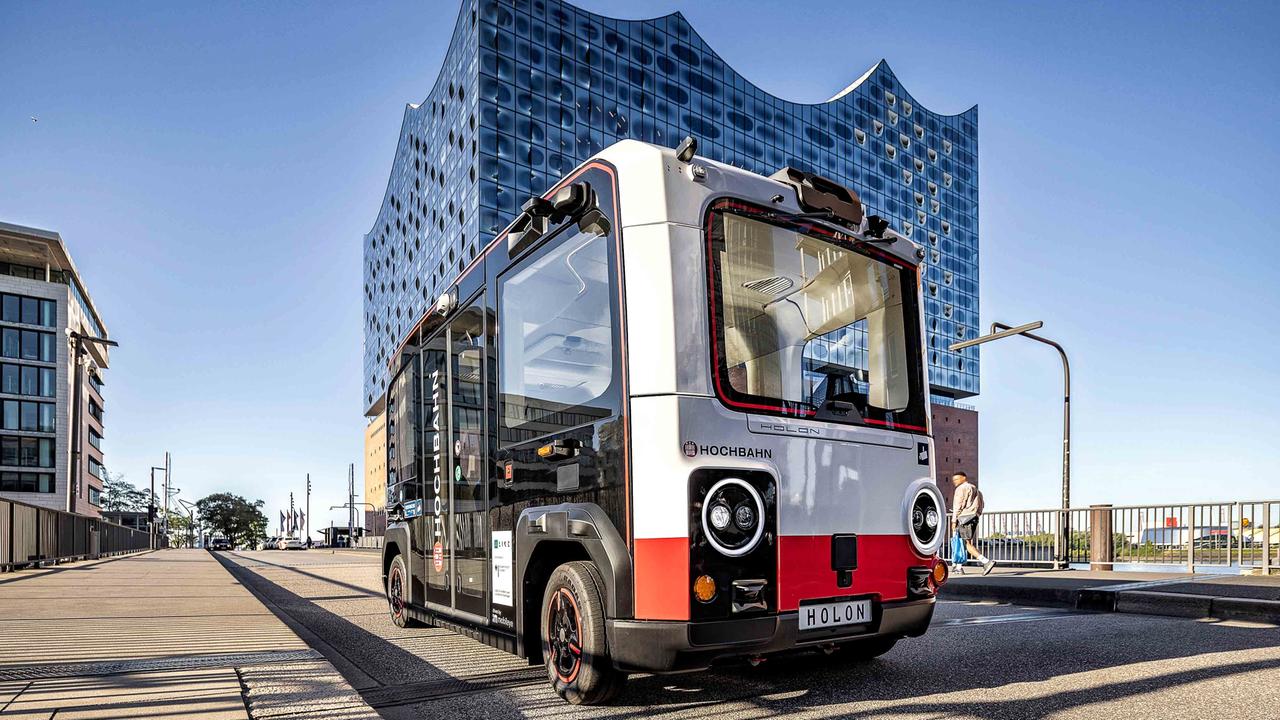 Vor der Elbphilharmonie in Hamburg steht ein weiß-rotes Elektro-Shuttle vom Typ "Holon urban".