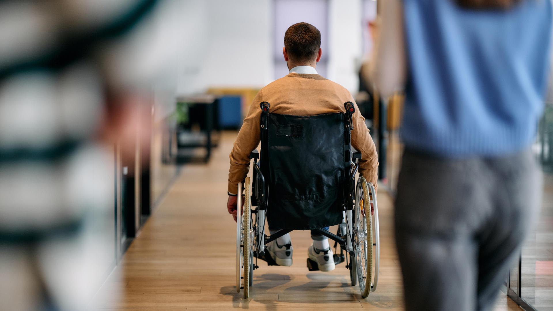 Ein Mann in einem Rollstuhl bewegt sich selbstständig durch einen modernen Bürokorridor.
