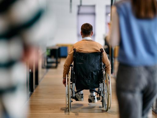 Ein Mann in einem Rollstuhl bewegt sich selbstständig durch einen modernen Bürokorridor.