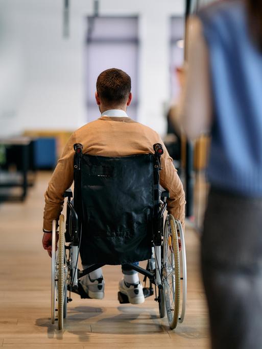 Ein Mann in einem Rollstuhl bewegt sich selbstständig durch einen modernen Bürokorridor.