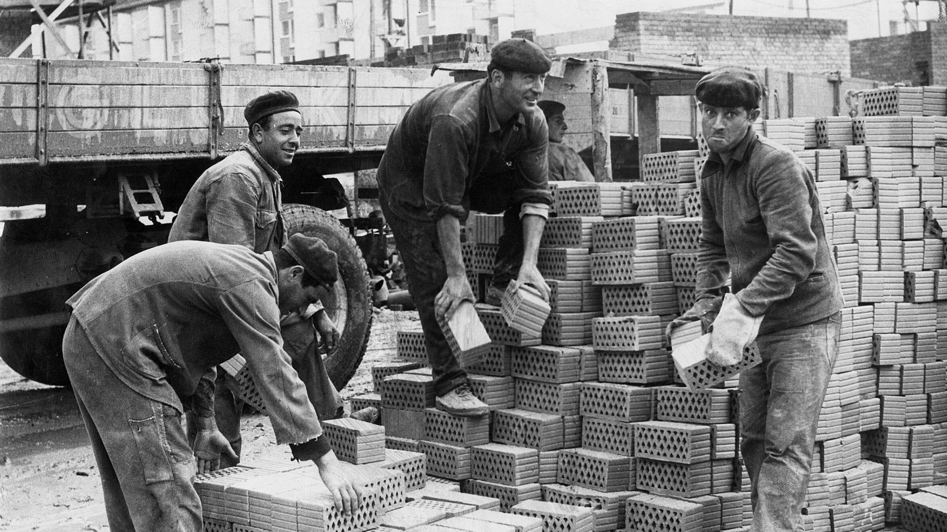 4 Männer helfen auf einer Baustelle. Sie tragen Steine. 