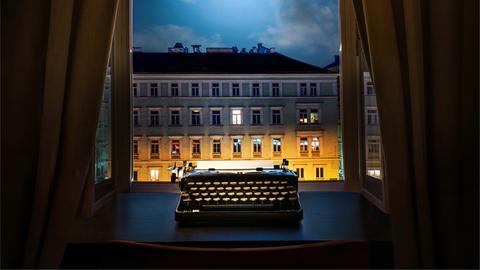 Eine Schreibmaschine steht nachts auf einem Schreibtisch vor dem geöffneten Fenster.