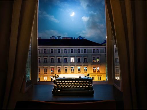 Eine Schreibmaschine steht nachts auf einem Schreibtisch vor dem geöffneten Fenster.