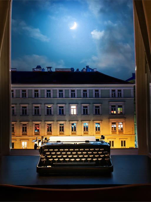 Eine Schreibmaschine steht nachts auf einem Schreibtisch vor dem geöffneten Fenster.