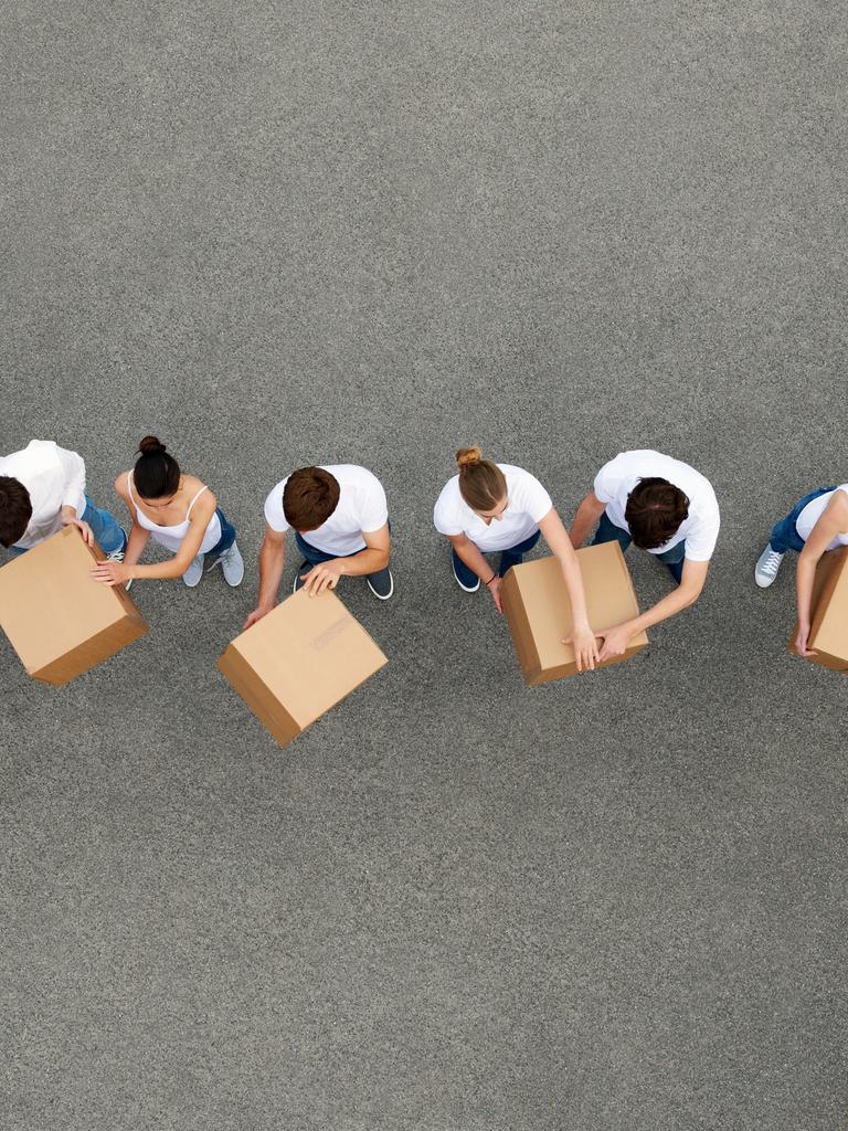 Luftaufnahme von Personen die sich Kartons gegenseitig weiterreichen. Die Personen tragen weiße T-Shirts und stehen auf einem grauen Betongrund.