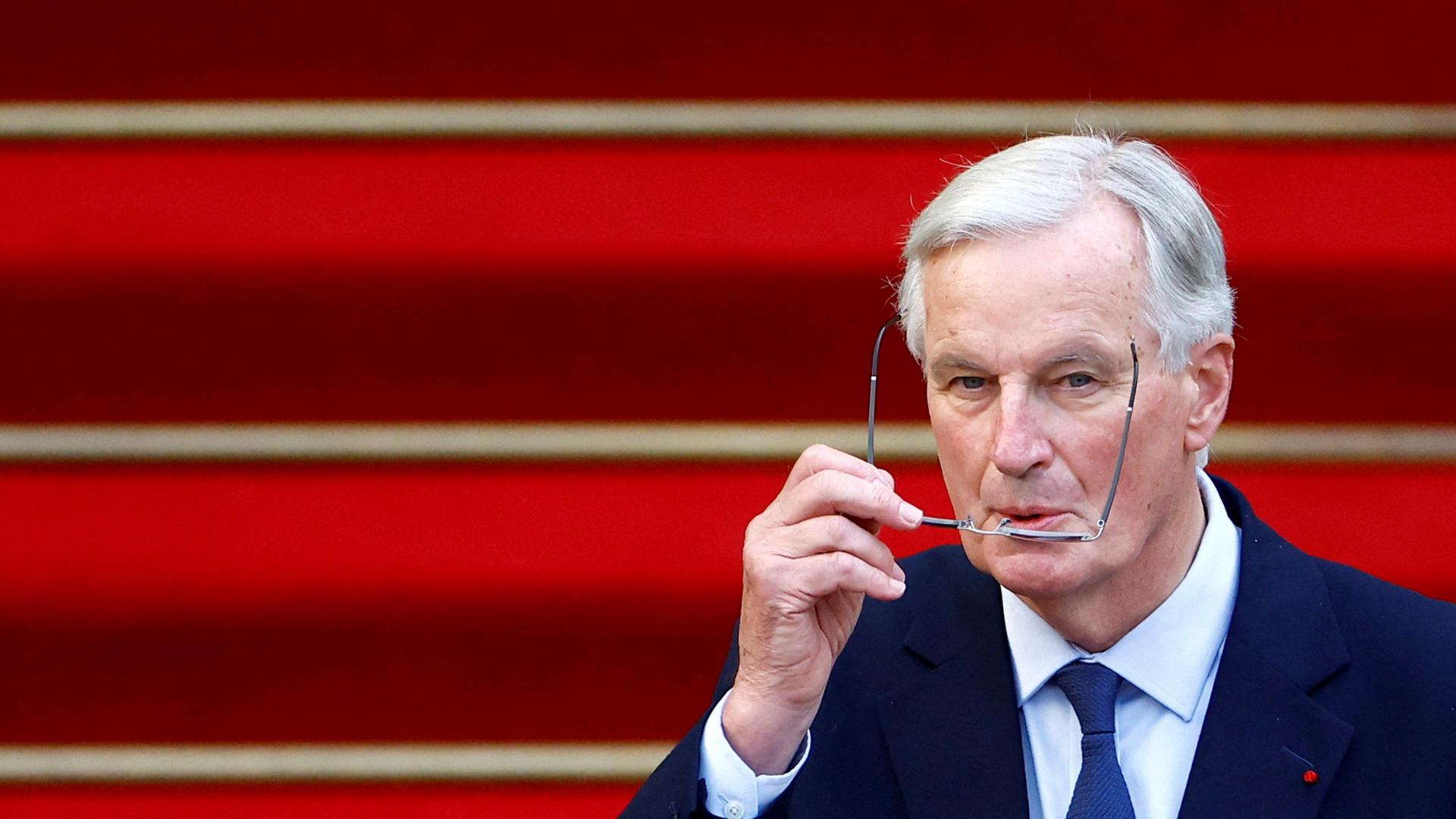 Der neue französische Premierminister Michel Barnier nimmt an der Übergabezeremonie teil. Vor einem roten Teppich nimmt er seine Brille von der Nase.