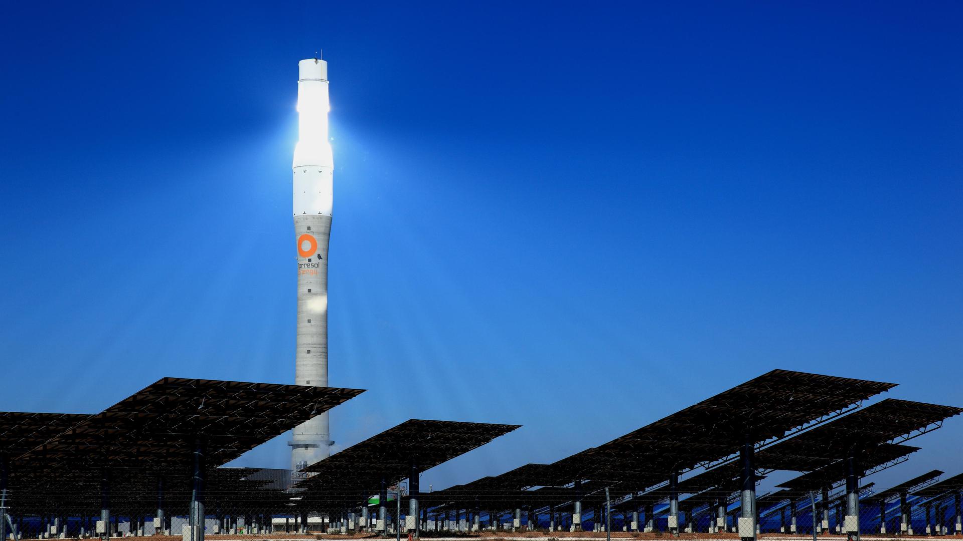 Ein hell erleuchteter Turm steht in der Nacht, davor Solarpanels.