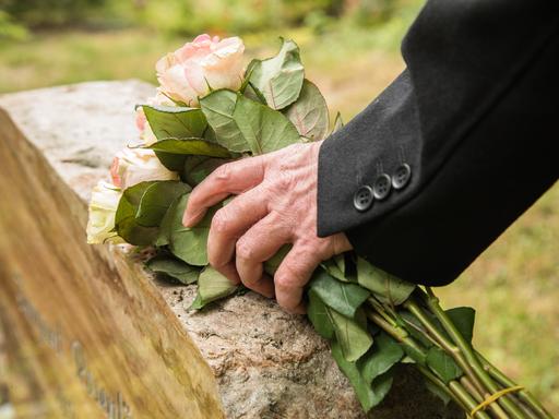 Ein älterer Mann legt in Berlin einen Strauß Rosen auf einen Grabstein (gestellte Szene)
