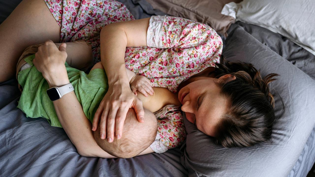 Eine Frau liegt engumschlungen mit einem Baby auf einem Bett und stillt es.