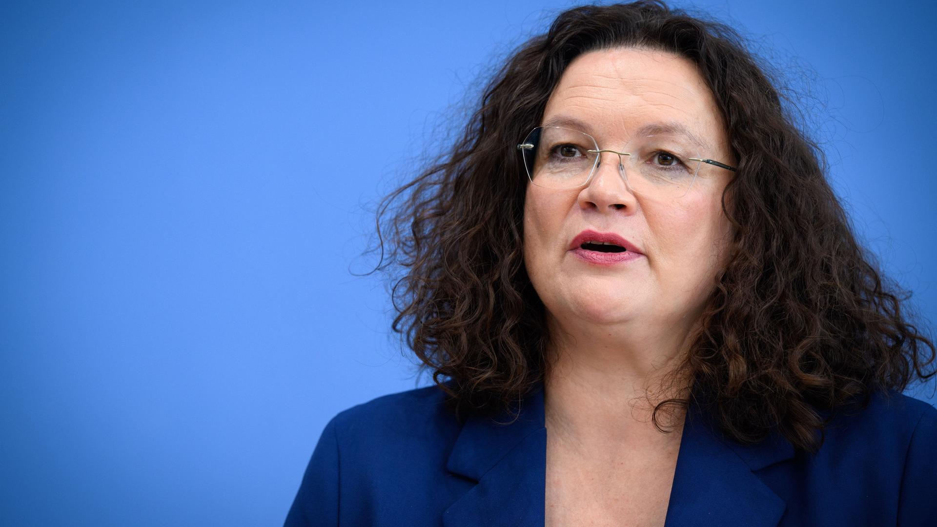 Andrea Nahles, Vorstandsvorsitzende der Bundesagentur für Arbeit sitzt vor blauem Hintergrund.