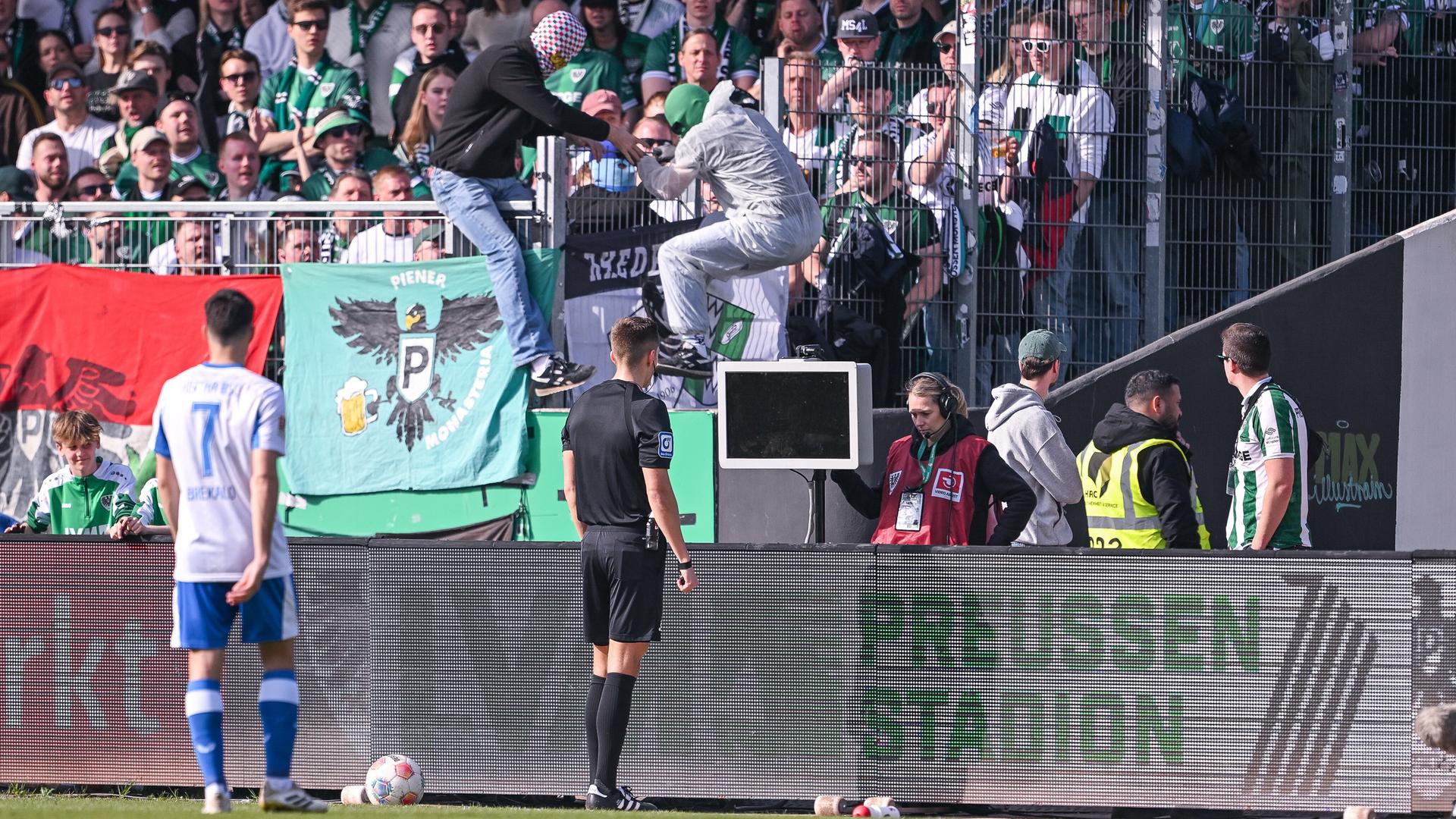 2. Bundesliga, Preußen Münster - Hertha BSC: Zwei Vermummte springen über die Bande als sich Schiedsrichter Felix Bickel die Szene ansehen will.