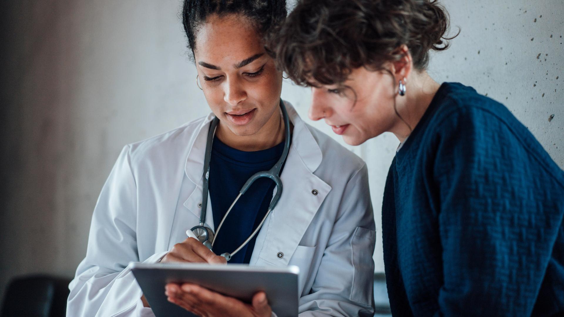 Eine Ärztin und eine Patientin schauen gemeinsam auf ein Tablet, das die Ärztin in der Hand hält.