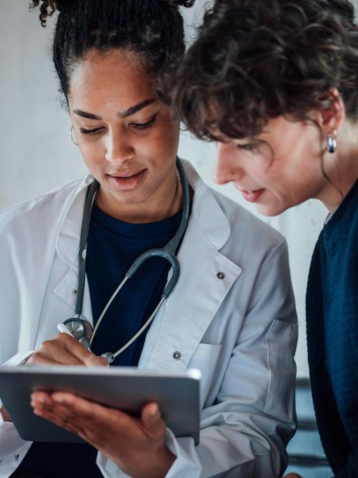 Eine Ärztin und eine Patientin schauen gemeinsam auf ein Tablet, das die Ärztin in der Hand hält.