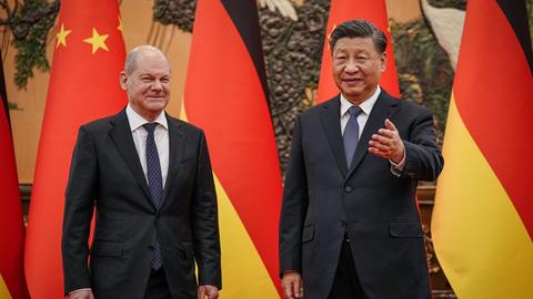 Bundeskanzler Scholz steht neben dem chinesischen Staatspräsidenten Xi. Im Hintergrund sieht man die Flaggen ihrer beiden Länder.