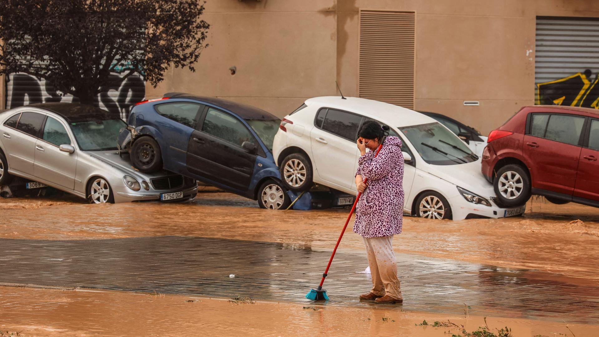 Nach Starkregen sind bei heftige Überschwemmungen in Spanien am 30. Oktober 2024 mehr als 90 Menschen getötet worden. Eine Frau in Valencia bei Aufräumarbeiten. Im Hintergrund aufeinandergestapelte Autos.