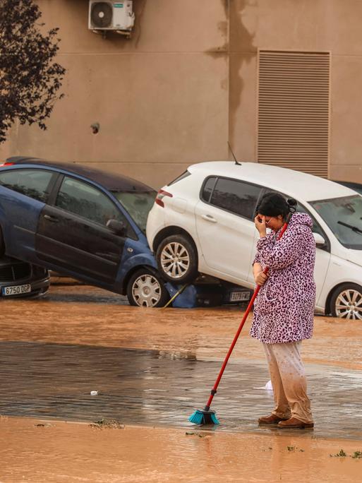 Nach Starkregen sind bei heftige Überschwemmungen in Spanien am 30. Oktober 2024 mehr als 90 Menschen getötet worden. Eine Frau in Valencia bei Aufräumarbeiten. Im Hintergrund aufeinandergestapelte Autos.