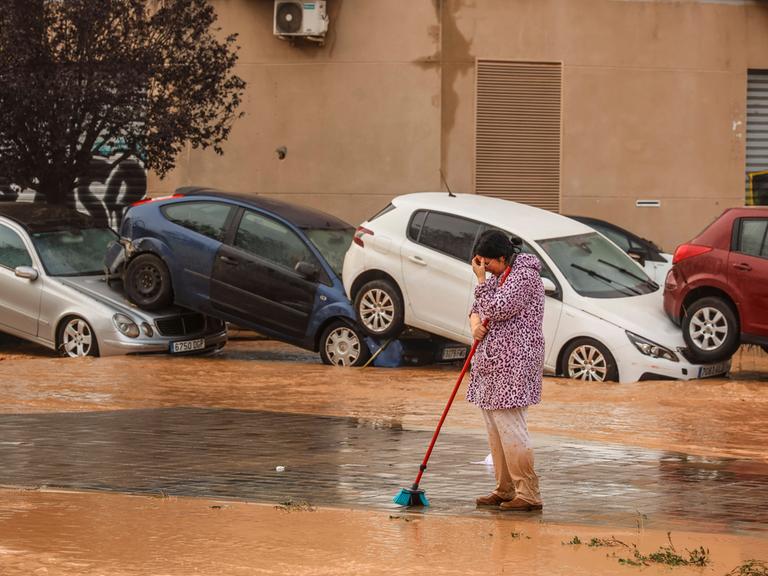 Nach Starkregen sind bei heftige Überschwemmungen in Spanien am 30. Oktober 2024 mehr als 90 Menschen getötet worden. Eine Frau in Valencia bei Aufräumarbeiten. Im Hintergrund aufeinandergestapelte Autos.