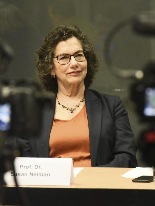 Prof. Susan Neiman aitzt an einem Tisch mit Namensschild. Im Vordergrund steht eine Fernsehkamera