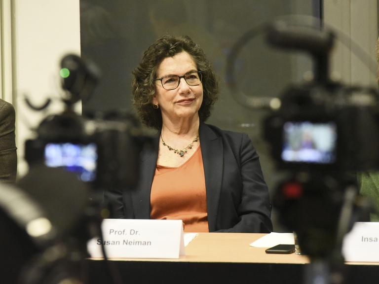 Prof. Susan Neiman aitzt an einem Tisch mit Namensschild. Im Vordergrund steht eine Fernsehkamera