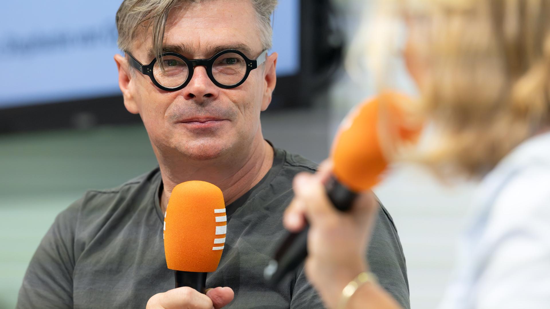 Jaroslav Rudiš trägt eine schwarze umrandete Brille und hält ein Mikrofon in der Hand. Ihm gegenüber sitzt mit Stephanie von Oppen, die ebenfalls ein Mikrofon in der Hand hält.