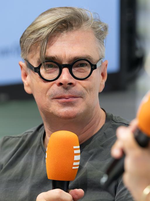 Jaroslav Rudiš trägt eine schwarze umrandete Brille und hält ein Mikrofon in der Hand. Ihm gegenüber sitzt mit Stephanie von Oppen, die ebenfalls ein Mikrofon in der Hand hält.