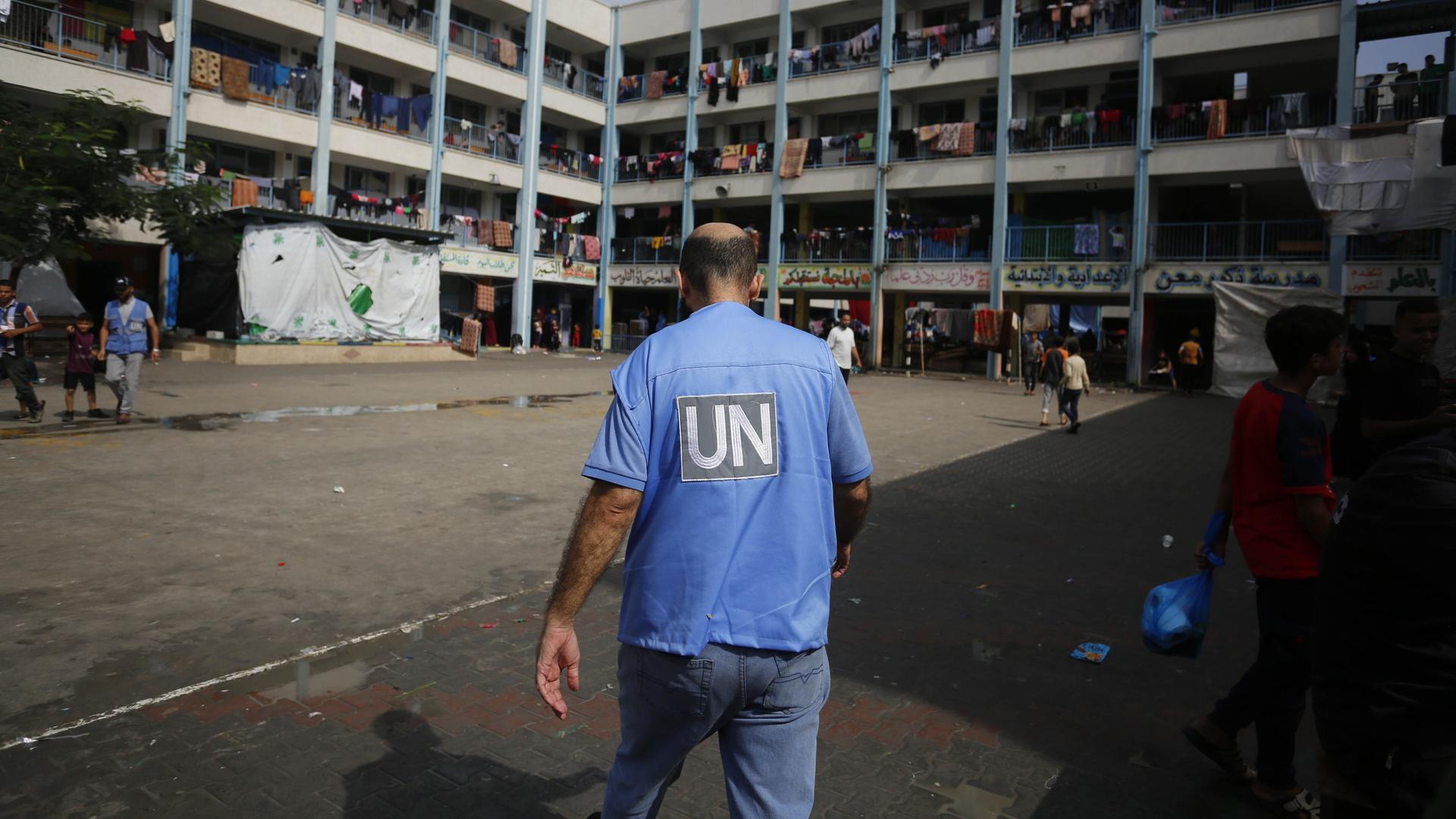 Ein UN-Mitarbeiter läuft über den Hof einer Schule in Gaza, in der flüchtige Familien untergekommen sind. Wäschestücke hängen über den Balkongeländern des Gebäudes.