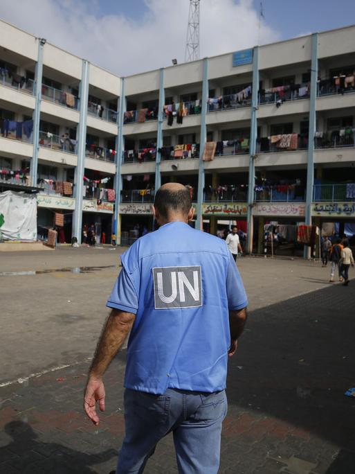 Ein UN-Mitarbeiter läuft über den Hof einer Schule in Gaza, in der flüchtige Familien untergekommen sind. Wäschestücke hängen über den Balkongeländern des Gebäudes.