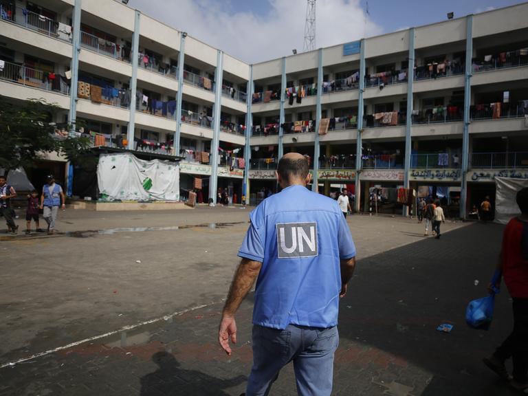 Ein UN-Mitarbeiter läuft über den Hof einer Schule in Gaza, in der flüchtige Familien untergekommen sind. Wäschestücke hängen über den Balkongeländern des Gebäudes.