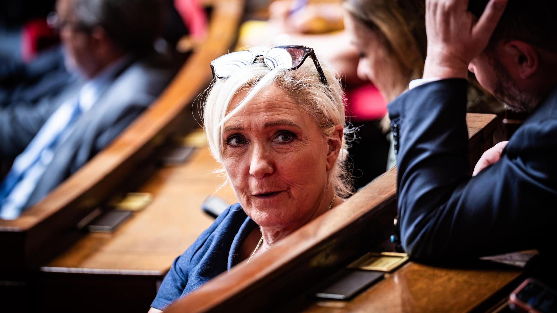 Die französische Politikerin Marine Le Pen in der französischen Nationalversammlung. Sie trägt ein blaues Oberteil, hat ihre Brille ins Haar gesteckt und schaut in die Kamera. Die französische Politikerin Marine Le Pen in der französischen Nationalversammlung. Sie trägt ein blaues Oberteil, hat ihre Brille ins Haar gesteckt und schaut in die Kamera.