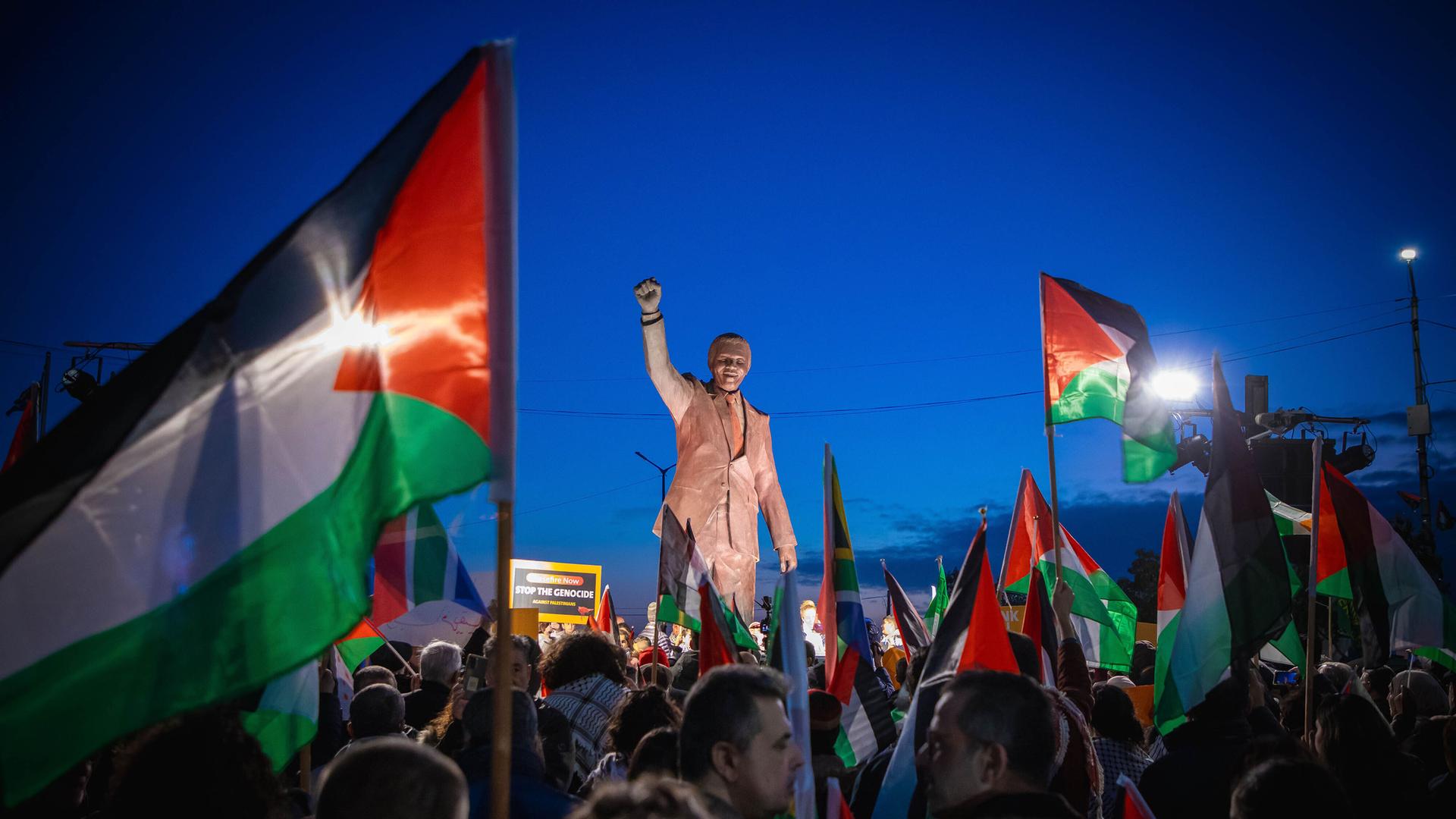 Palästinenser mit Fahnen und Spruchbändern auf dem Nelson-Mandela-Platz mit Mandela-Statue mit geregter Faust in Ramallah im Westjordanland. Anlass war die von der Republik Südafrika beim Internationalen Gerichtshof (IGH) eingereichte Klage wegen mutmaßlichen Völkermords gegen Israel.