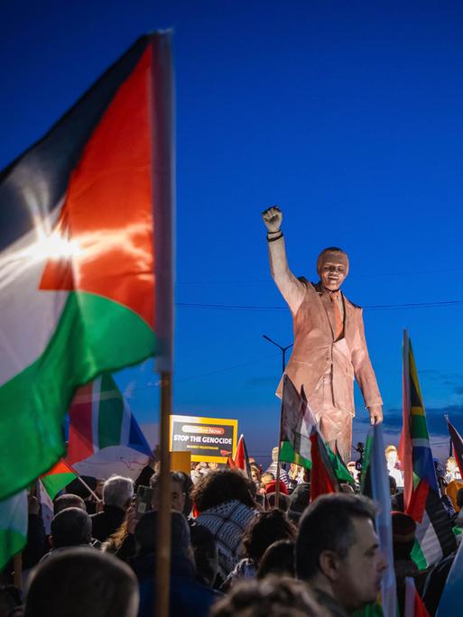 Palästinenser mit Fahnen und Spruchbändern auf dem Nelson-Mandela-Platz mit Mandela-Statue mit geregter Faust in Ramallah im Westjordanland. Anlass war die von der Republik Südafrika beim Internationalen Gerichtshof (IGH) eingereichte Klage wegen mutmaßlichen Völkermords gegen Israel.