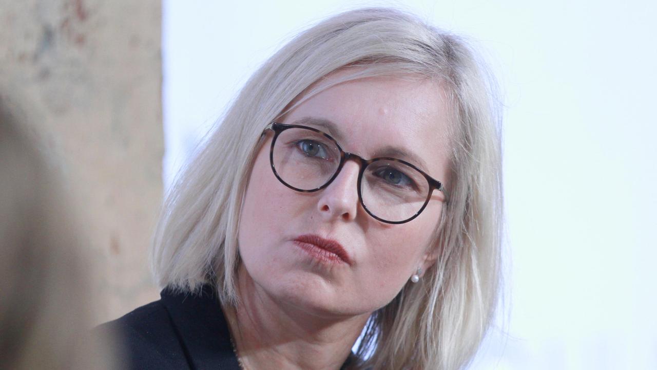 Das Bild zeigt Christiane Schenderlein mit ernstem Gesichtsausdruck. Sie trägt eine schwarze Hornbrille, schwarzen Blazer und eine Kette.