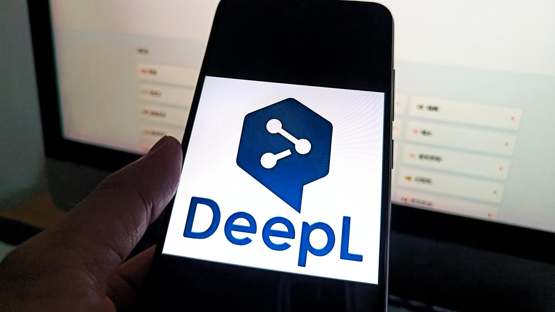 Auf einem Smartphone ist das Logo von DeepL zu sehen, dahinter ist ein Bildschirm. Auf einem Smartphone ist das Logo von DeepL zu sehen, dahinter ist ein Bildschirm.