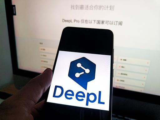Auf einem Smartphone ist das Logo von DeepL zu sehen, dahinter ist ein Bildschirm. Auf einem Smartphone ist das Logo von DeepL zu sehen, dahinter ist ein Bildschirm.