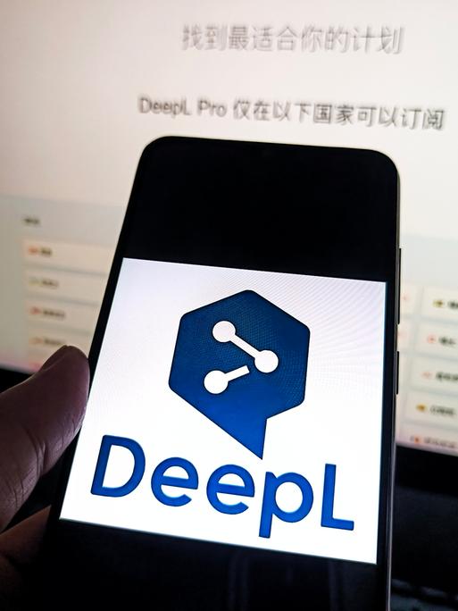 Auf einem Smartphone ist das Logo von DeepL zu sehen, dahinter ist ein Bildschirm. Auf einem Smartphone ist das Logo von DeepL zu sehen, dahinter ist ein Bildschirm.