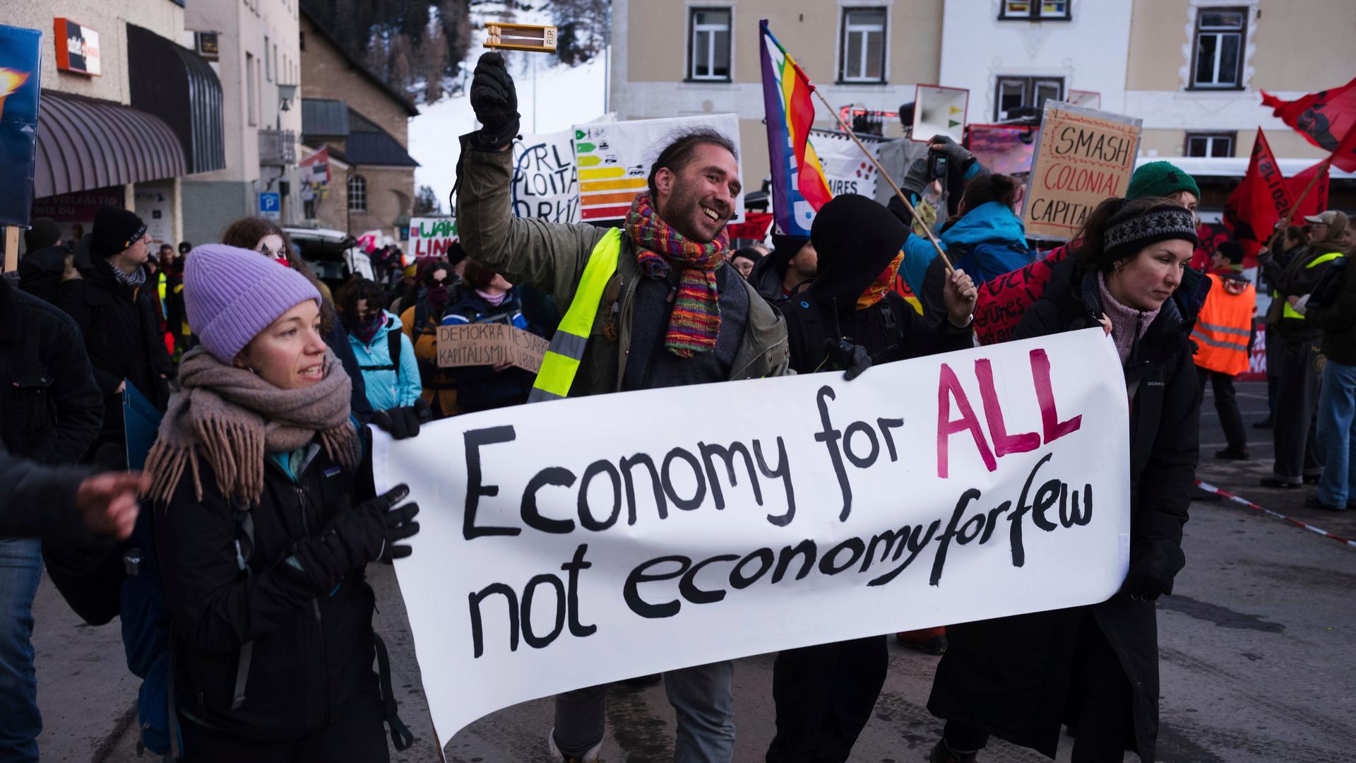 Demonstrierende halten in Plakat mit der Aufschrift "Economy for all not economy for few", also in etwa "Wirtschaft für alle nicht für wenige".