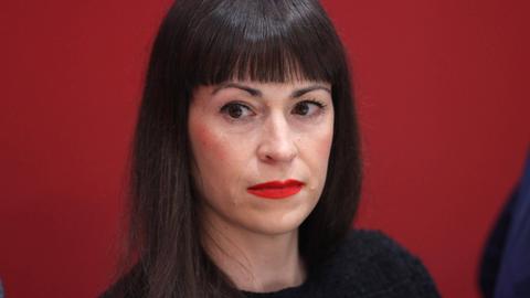 Eine Frau mit schulterlangen braunen Haaren blickt in die Kamera. Hinter ihr ist eine rote Wand. Es ist die Sprachsoziologin Carolin Amlinger.
