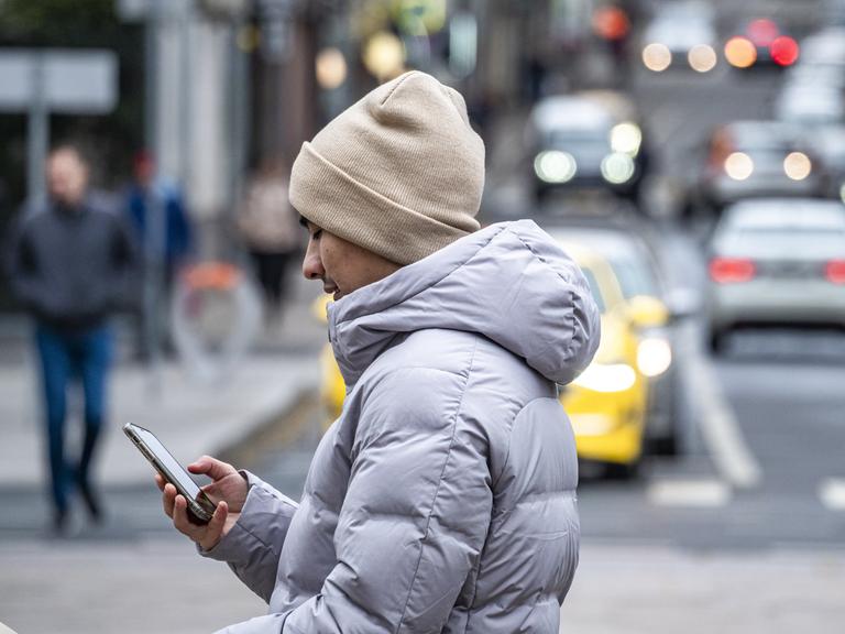 Ein Jugendlicher überquert eine Straße und schaut dabei auf sein Smartphone.