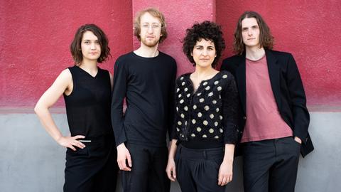 Auf dem Gruppenfoto stehen zwei Männer und zwei Frauen vor einer rosaroten Wand und schauen in die Kamera.