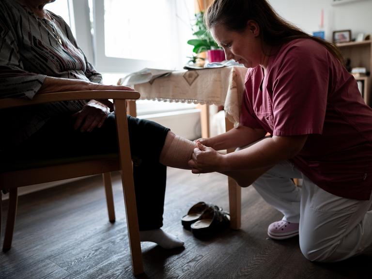 Eine Pflegerin zieht einer älteren Frau einen Stützstrumpf an