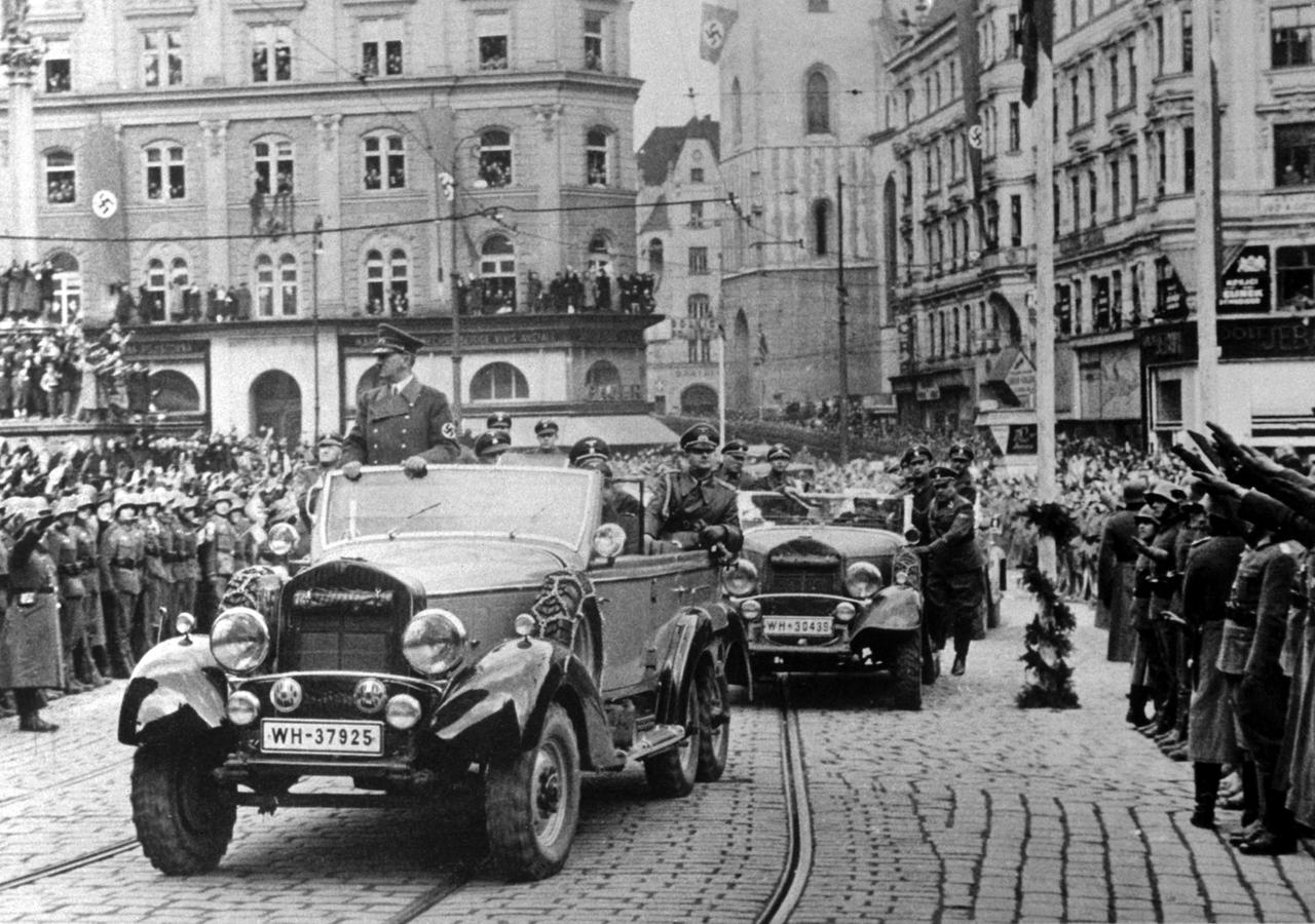 Historisches Foto von Adolf Hitler, der in einem offenen Wagen stehend durch Brünn fährt. Menschenmengen haben sich versammelt.