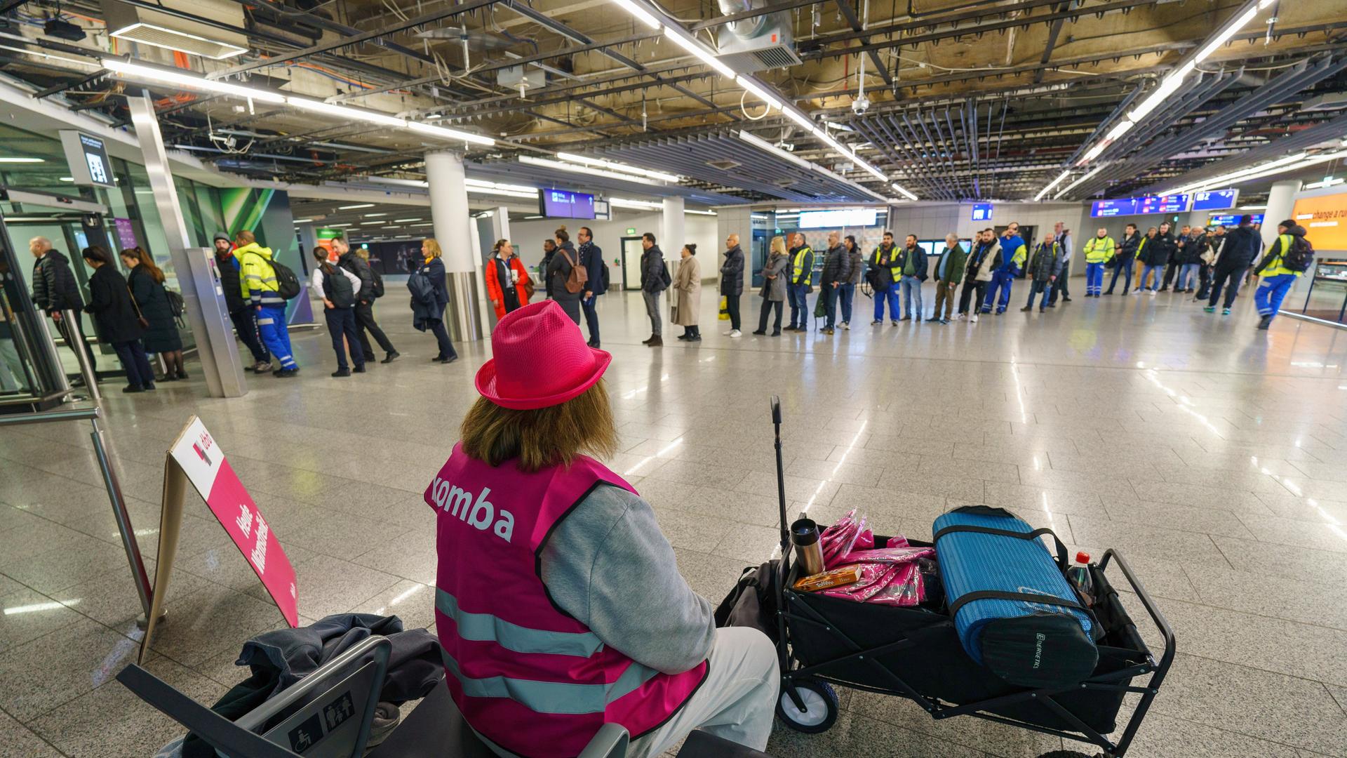 Frankfurt/Main: Eine Vertreterin der Komba-Gewerkschaft (Kommunalbeamte und Arbeitnehmer im Deutschen Beamtenbund) sitzt am Flughafen während im Hintergrund Flughafen-Beschäftigte zur Sicherheitskontrolle anstehen. Frankfurt/Main: Eine Vertreterin der Komba-Gewerkschaft (Kommunalbeamte und Arbeitnehmer im Deutschen Beamtenbund) sitzt am Flughafen während im Hintergrund Flughafen-Beschäftigte zur Sicherheitskontrolle anstehen.