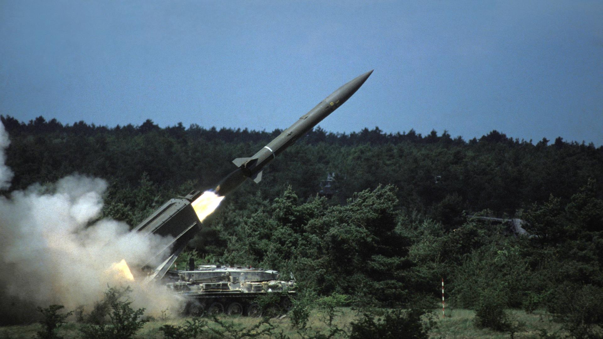 Aus einem großen Armeefahrzeug wird eine französische Atomrakete abgefeuert. Drum herum Büsche und grüne Natur.