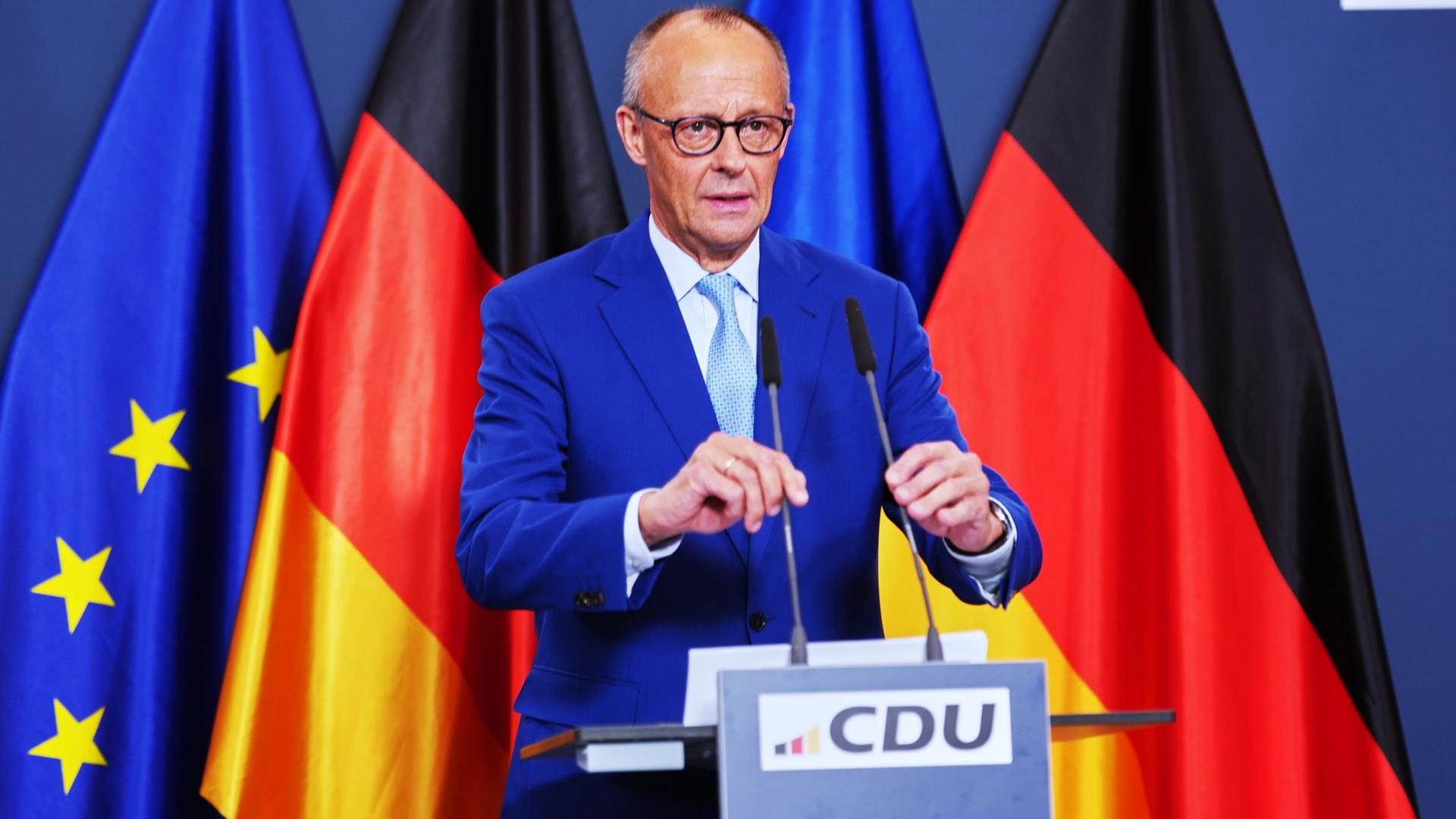 Bundeskanzler Friedrich Merz steht an einem Rednerpult und rückt zwei Mikrofone zurecht. Im Hintergrund sind die Flaggen der Bundesrepublik und der Europäischen Union aufgestellt. Bundeskanzler Friedrich Merz steht an einem Rednerpult und rückt zwei Mikrofone zurecht. Im Hintergrund sind die Flaggen der Bundesrepublik und der Europäischen Union aufgestellt.