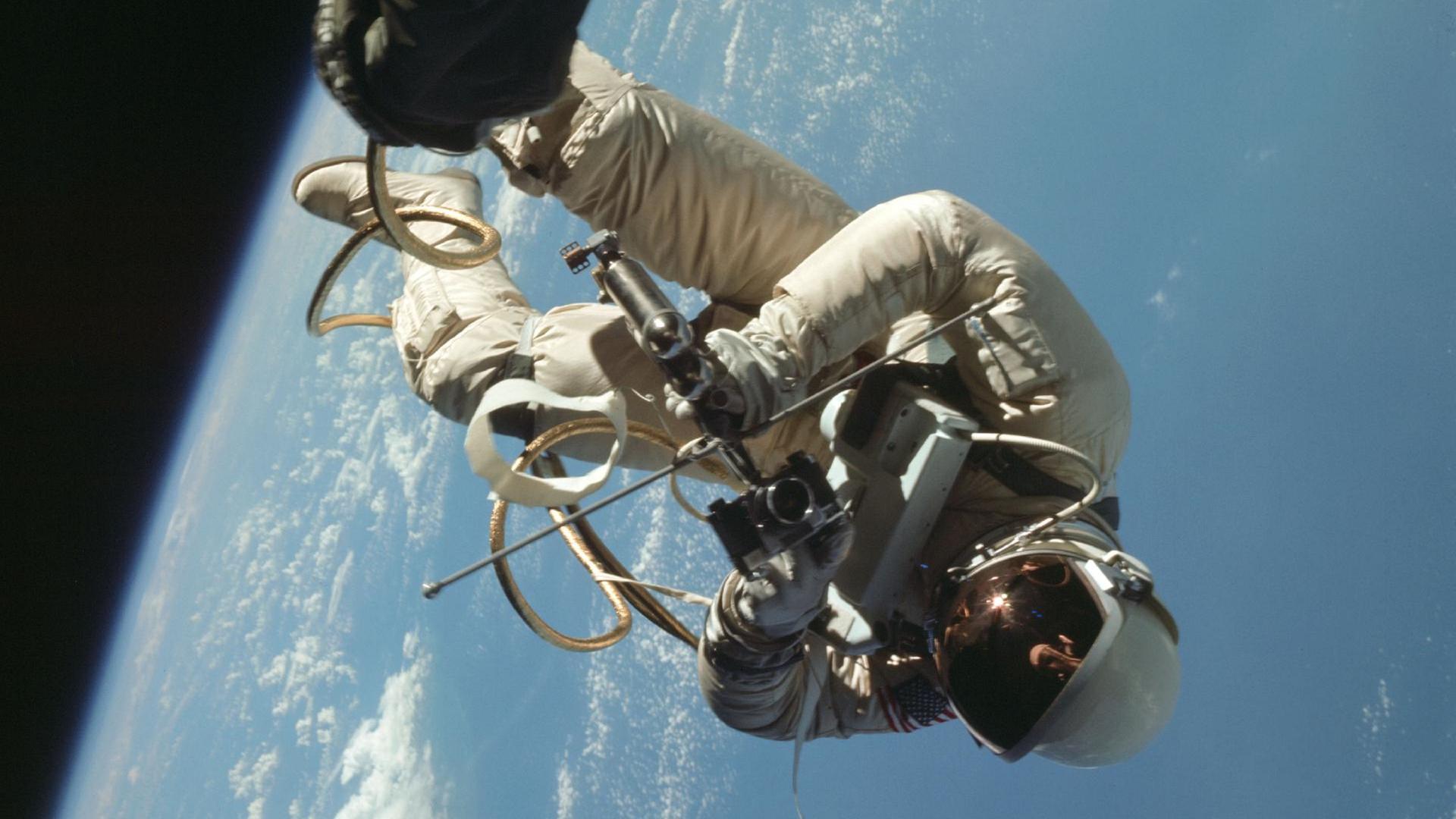 Der Astronaut Ed White schwebt außerhalb des Raumschiffs im All. Im Hintergrund ist die Erde zu sehen.