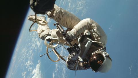 Der Astronaut Ed White schwebt außerhalb des Raumschiffs im All. Im Hintergrund ist die Erde zu sehen.