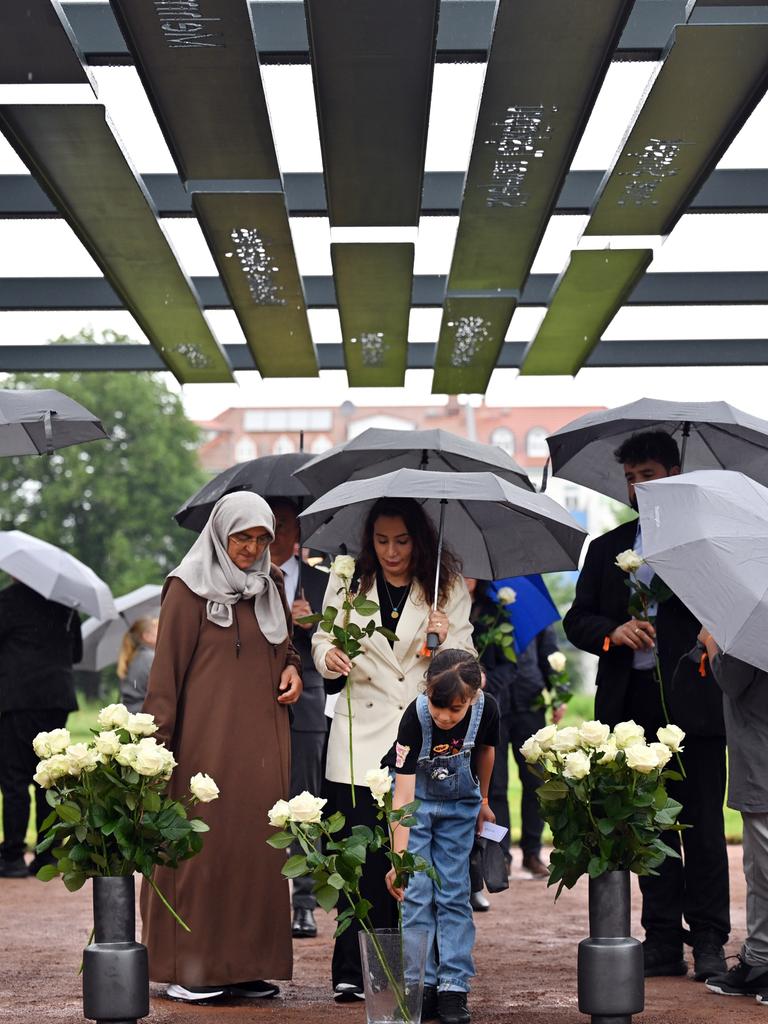 Mehrere Menschen mit Schirmen stehen unter einem aus Stahlbögen bestehenden Mahnmal, an denen die Namen und Biografien der NSU-Opfer zu lesen sind. Mehrere Menschen mit Schirmen stehen unter einem aus Stahlbögen bestehenden Mahnmal, an denen die Namen und Biografien der NSU-Opfer zu lesen sind.